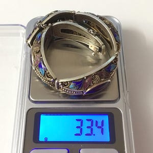 May include: Two silver bracelets with blue, purple, and pink enamel floral designs. The bracelets are on a digital scale that reads 33.4 grams.