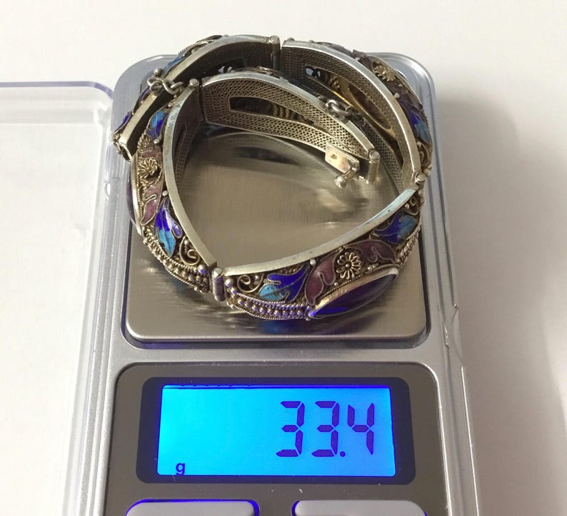 May include: Two silver bracelets with blue, purple, and pink enamel floral designs. The bracelets are on a digital scale that reads 33.4 grams.
