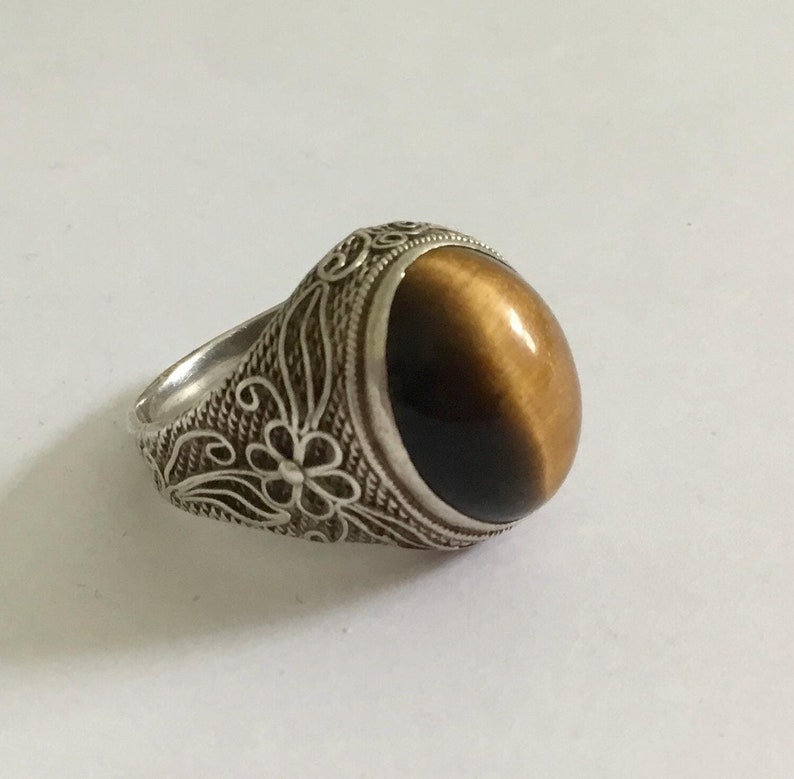 May include: A silver ring with an ornate floral design and a brown tiger's eye gemstone.