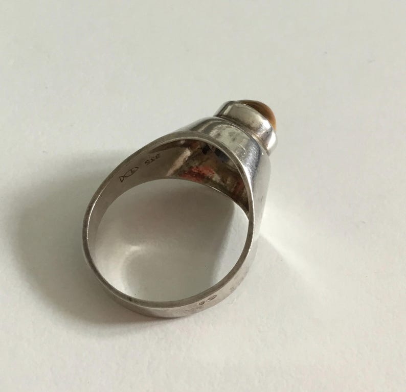 May include: Silver ring with a brown gemstone set in a dome-shaped setting. The ring is marked "925" and "D.C.S."
