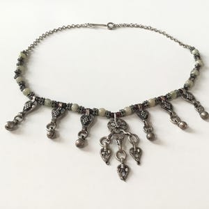 Op de afbeelding: Een zilverkleurige ketting met een fijne schakelketting versierd met lichtgroene kralen en kleine donkere tussenstukjes. Het sieraad bevat diverse bungelende zilverkleurige bedels met gedetailleerde filigraanpatronen en kleine bolletjes.
