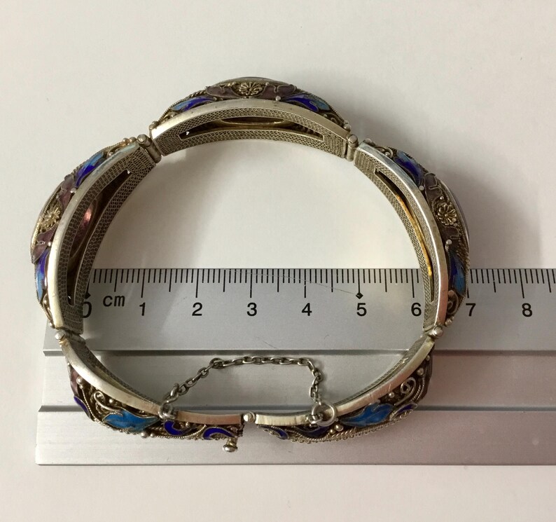 May include: A silver bracelet with blue and purple enamel and filigree detailing. The bracelet is 6 cm in length and has a chain closure.