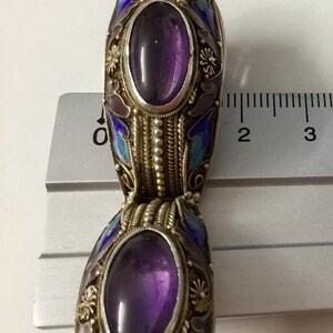 May include: A silver bracelet with two purple amethyst stones set in oval-shaped cloisonn&eacute; enamel. The enamel is decorated with blue, white, and pink floral designs.