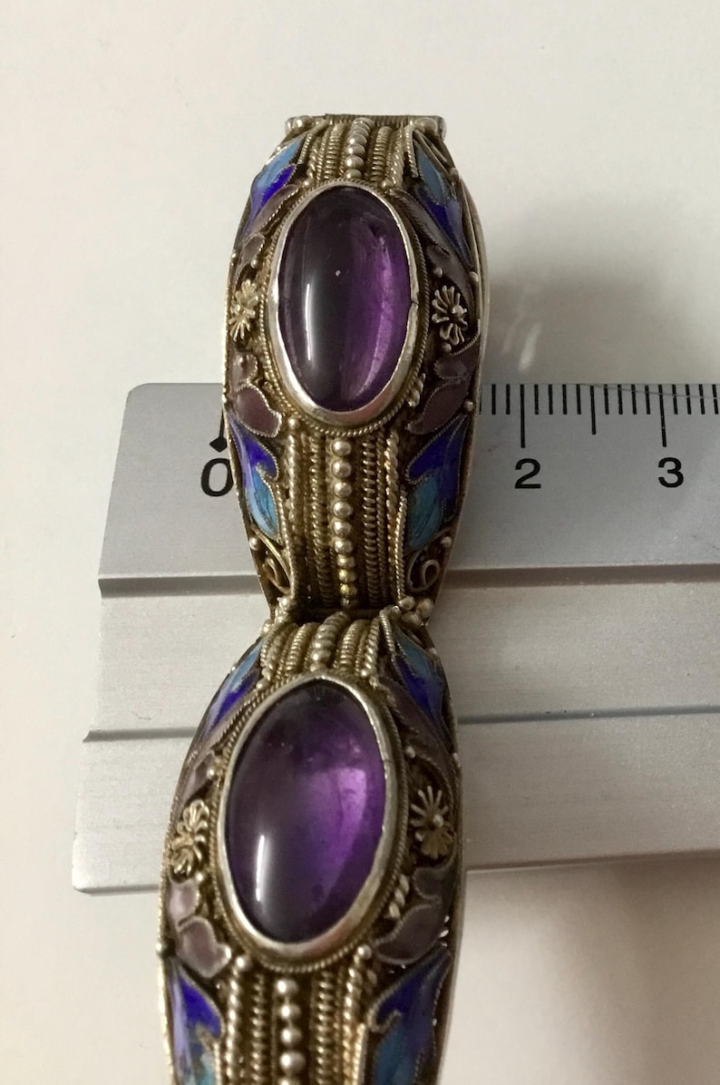 May include: A silver bracelet with two purple amethyst stones set in oval-shaped cloisonn&eacute; enamel. The enamel is decorated with blue, white, and pink floral designs.
