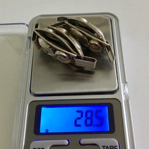 May include: A silver watch band with multiple links is on a digital scale that reads 28.5 grams.