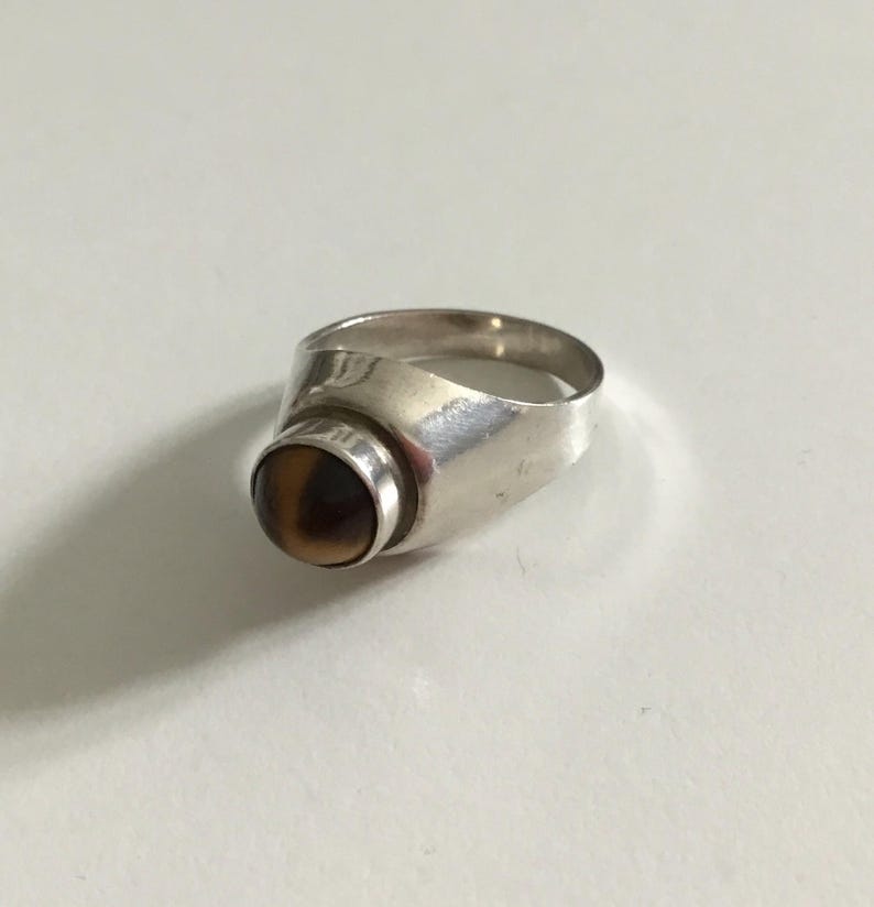 May include: A silver ring with a brown and black gemstone. The ring has a unique design with a rounded top and a smooth band.