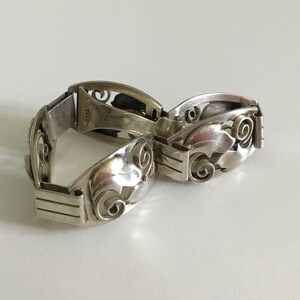 May include: A silver bracelet with a floral design. The bracelet is made of two pieces that connect with a clasp. The bracelet is marked "925" and "NIAS" on the inside.