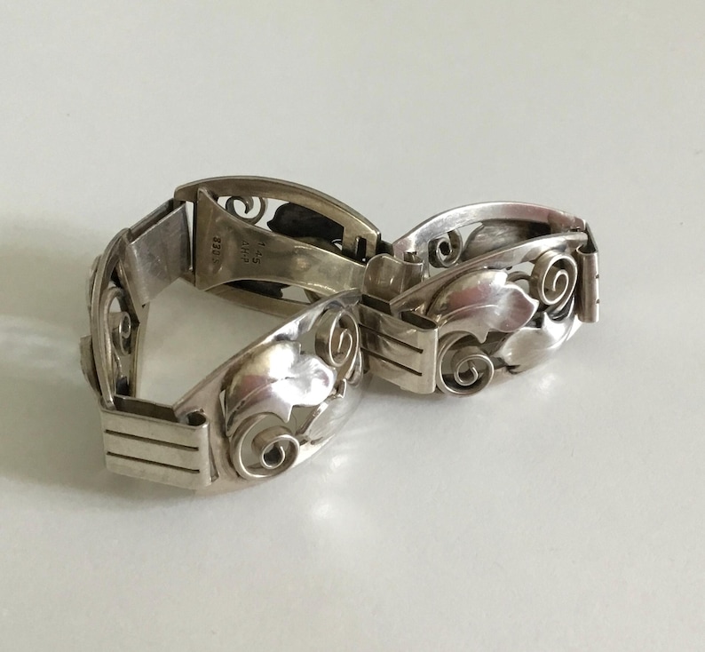 May include: A silver bracelet with a floral design. The bracelet is made of two pieces that connect with a clasp. The bracelet is marked "925" and "NIAS" on the inside.