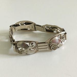 May include: A silver bracelet with an intricate floral design. The bracelet is made of sterling silver and has a clasp closure. The bracelet is approximately 7 inches in length.