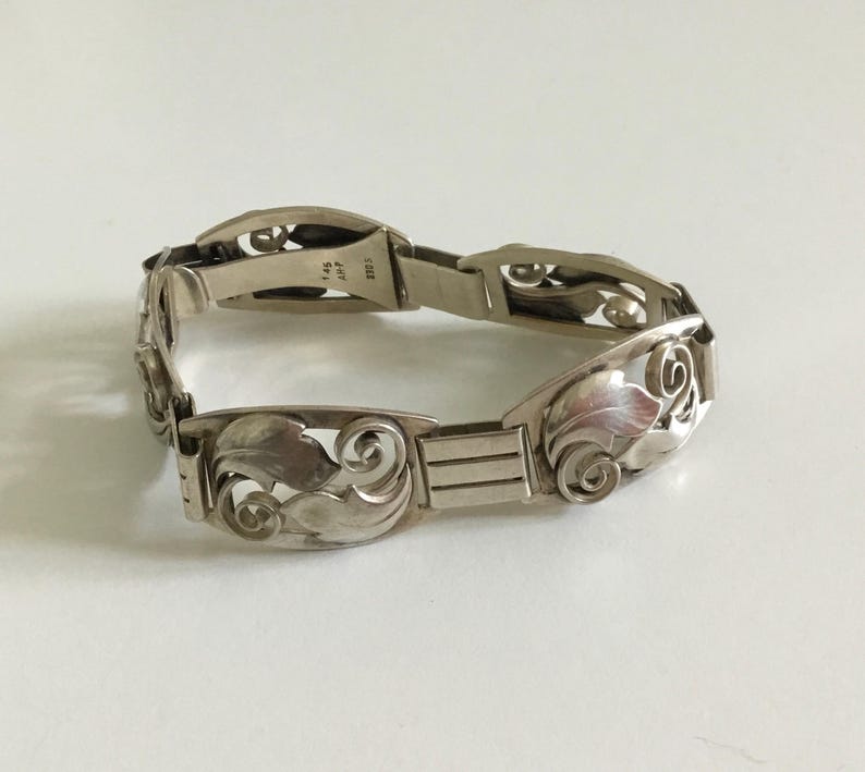 May include: A silver bracelet with an intricate floral design. The bracelet is made of sterling silver and has a clasp closure. The bracelet is approximately 7 inches in length.