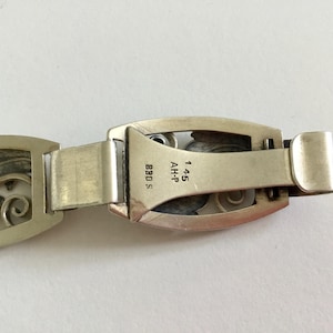 May include: Silver bracelet with an intricate floral design. The clasp has the markings "AH-P 14.5 830 S".