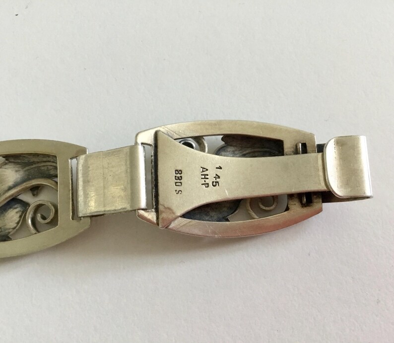 May include: Silver bracelet with an intricate floral design. The clasp has the markings "AH-P 14.5 830 S".