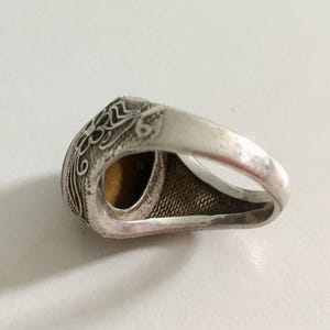 May include: Silver ring with an ornate design and a brown gemstone. The ring is set on a white background.