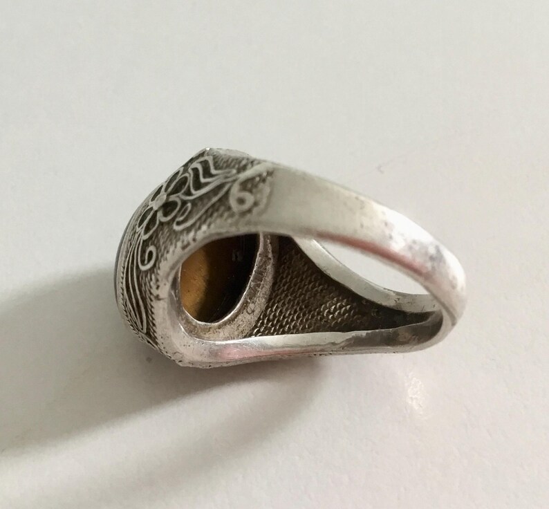 May include: Silver ring with an ornate design and a brown gemstone. The ring is set on a white background.