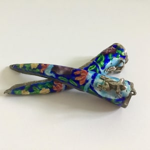 May include: A pair of antique silver chopsticks with blue and white enamel and floral designs. The chopsticks have a silver charm at the top.