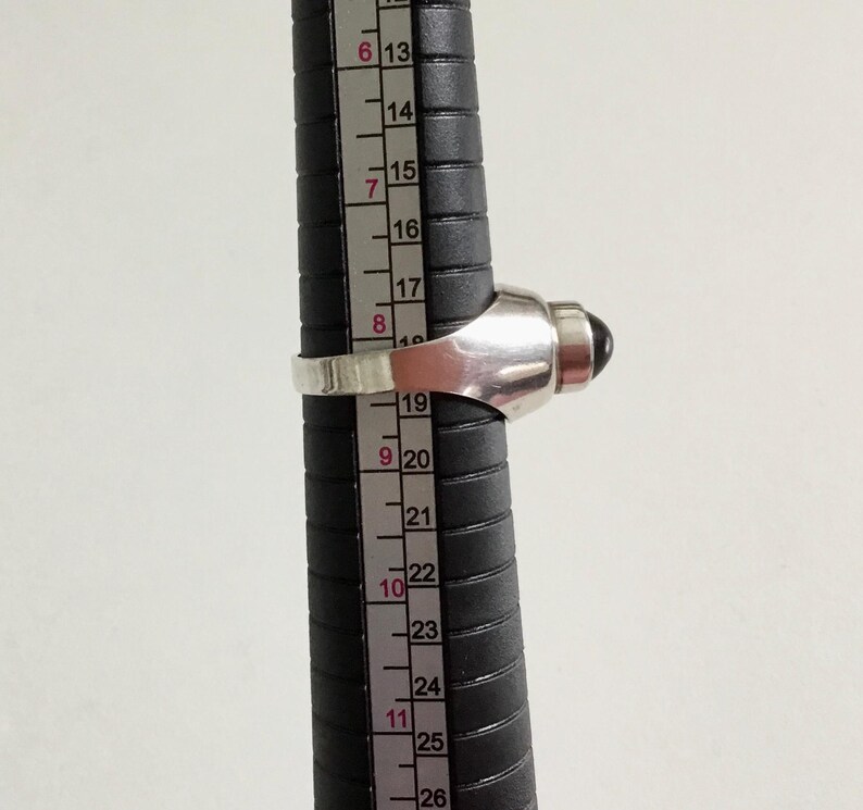 May include: A silver ring with a black gemstone set in a dome-shaped top. The ring is sized using a ruler, showing a size of 9.