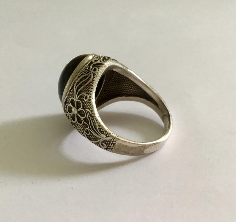 May include: A silver ring with an ornate floral design and a brown tiger's eye stone.