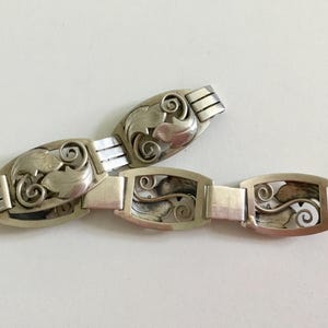 May include: A silver bracelet with a delicate, intricate design of leaves and swirls. The bracelet is made of multiple linked sections, each featuring a unique pattern.