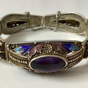 May include: A silver bracelet with an amethyst stone and blue and purple enamel floral designs.