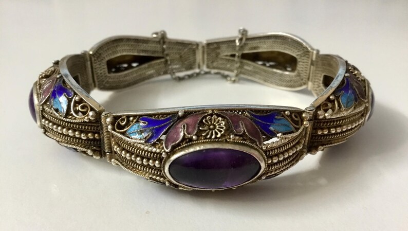 May include: A silver bracelet with an amethyst stone and blue and purple enamel floral designs.