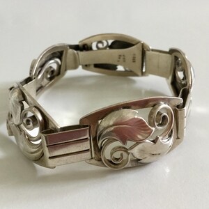 May include: A silver bracelet with an intricate design of leaves and swirls. The bracelet is made of sterling silver and has a clasp closure.