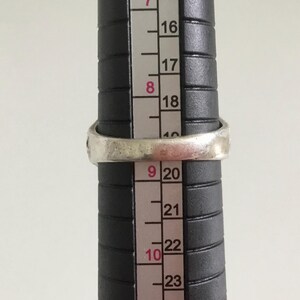 May include: A silver ring with a textured band, measured against a ruler with markings from 16 to 23.
