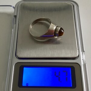 May include: A silver ring with a brown gemstone. The ring is on a digital scale that reads 4.7 grams.
