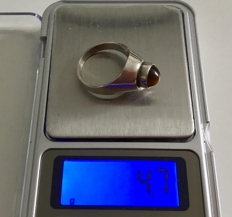 May include: A silver ring with a brown gemstone. The ring is on a digital scale that reads 4.7 grams.