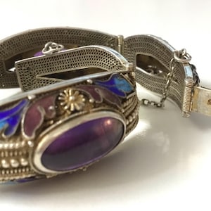 May include: A silver bracelet with an amethyst stone set in a silver and enamel frame. The bracelet is decorated with floral designs in blue and purple enamel. The clasp is marked "SILVER".