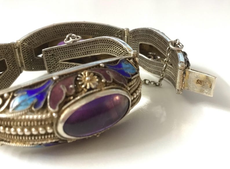 May include: A silver bracelet with an amethyst stone set in a silver and enamel frame. The bracelet is decorated with floral designs in blue and purple enamel. The clasp is marked "SILVER".