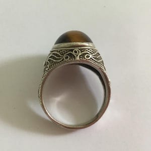 May include: A silver ring with an ornate design and a brown tiger's eye stone.