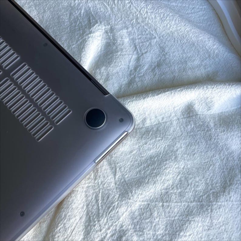 May include: The back of a silver laptop computer with a clear case. The laptop is sitting on a white fabric surface.