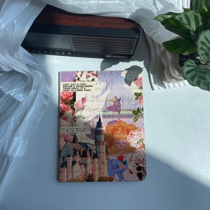 Könnte beinhalten: Eine dekorative Tablet-Hülle mit einer Märchenillustration, darunter ein Schloss, eine Prinzessin und florale Details. Die Hülle trägt den Text "THEY SAY IF YOU DREAM A THING MORE THAN ONCE, IT'S SURE TO COME TRUE."
