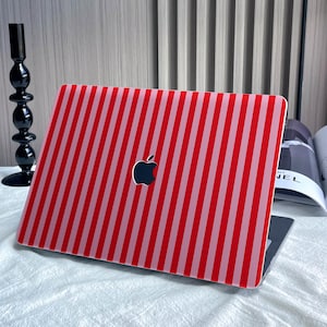 May include: A laptop featuring a red and white striped cover. The Apple logo is visible on the cover. The laptop is open on a white surface.