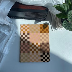 May include: A brown and beige checkered notebook with a black and white checkered pattern on the bottom. The notebook is lying flat on a white surface.