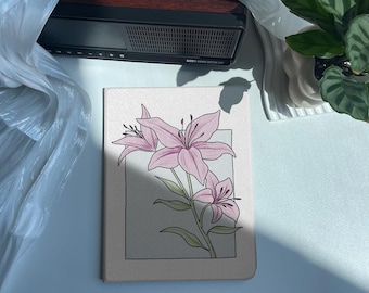 May include: A white canvas notebook with a pink and white floral illustration of lilies. The notebook is sitting on a white surface.