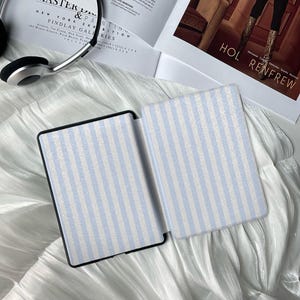 May include: Two open e-reader cases with a light blue and white striped pattern. The cases are on a white, textured surface. The text "HOL RENFREW" is visible in the background.