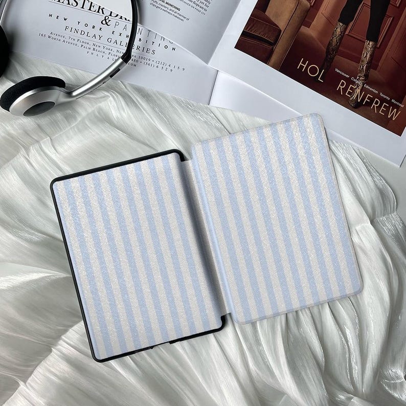 May include: Two open e-reader cases with a light blue and white striped pattern. The cases are on a white, textured surface. The text "HOL RENFREW" is visible in the background.