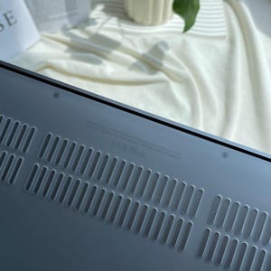 May include: The back of a silver laptop with a series of small ventilation holes.