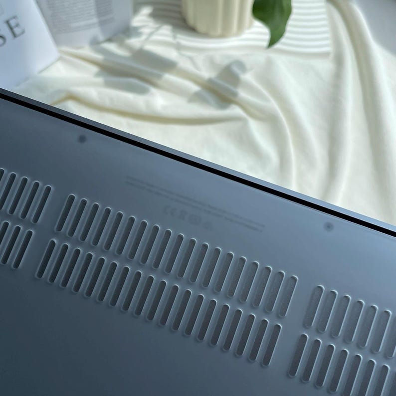 May include: The back of a silver laptop with a series of small ventilation holes.
