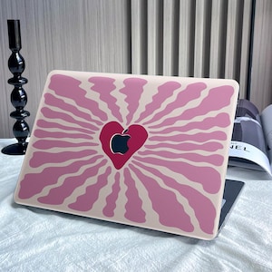 May include: A pink and beige laptop skin with a stylised heart design featuring an apple logo. The heart is in the centre of the design and is surrounded by radiating lines.