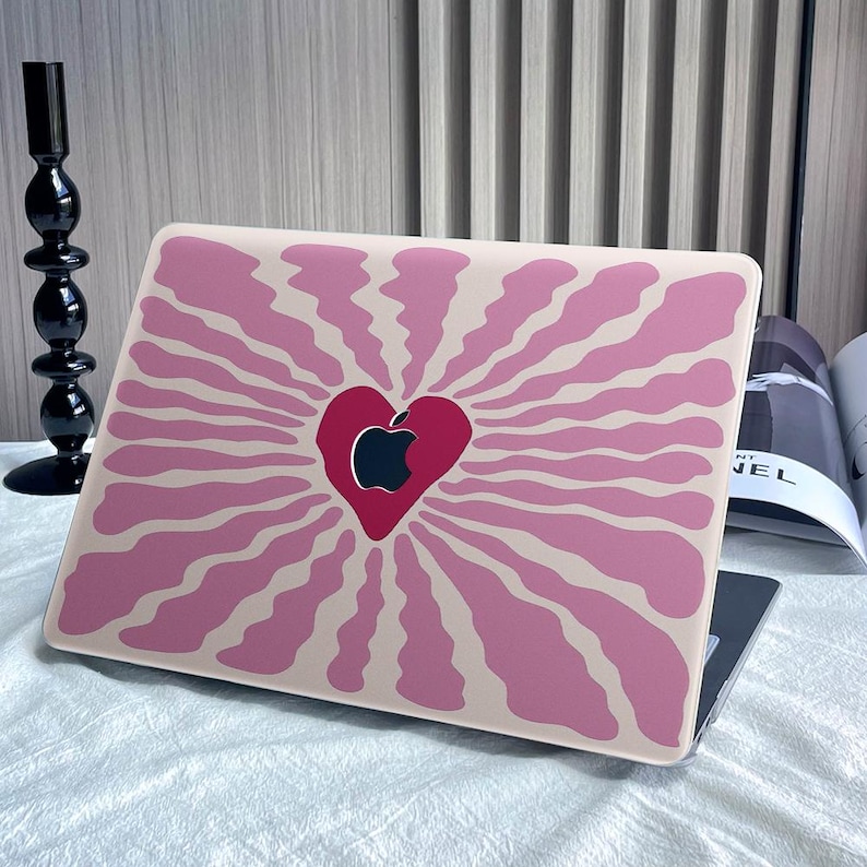 May include: A pink and beige laptop skin with a stylized heart design featuring an apple logo. The heart is in the center of the design and is surrounded by radiating lines.