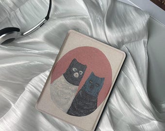 May include: A beige and brown e-reader cover with a red circle and two black cats wearing blue and white knitted hats.