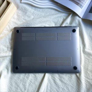 May include: The back of a silver laptop computer with a textured surface and two rubber feet.
