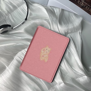 May include: A pink e-reader case with a cartoon hamster illustration. The case is made of a textured material.