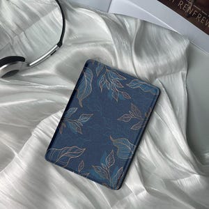 May include: A blue e-reader case with a gold leaf pattern. The case is made of a soft, durable material and has a sleek, modern design.