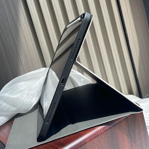 May include: A black iPad case with a built-in stand, shown in a folded position. The case is made of a durable material and has a sleek design.
