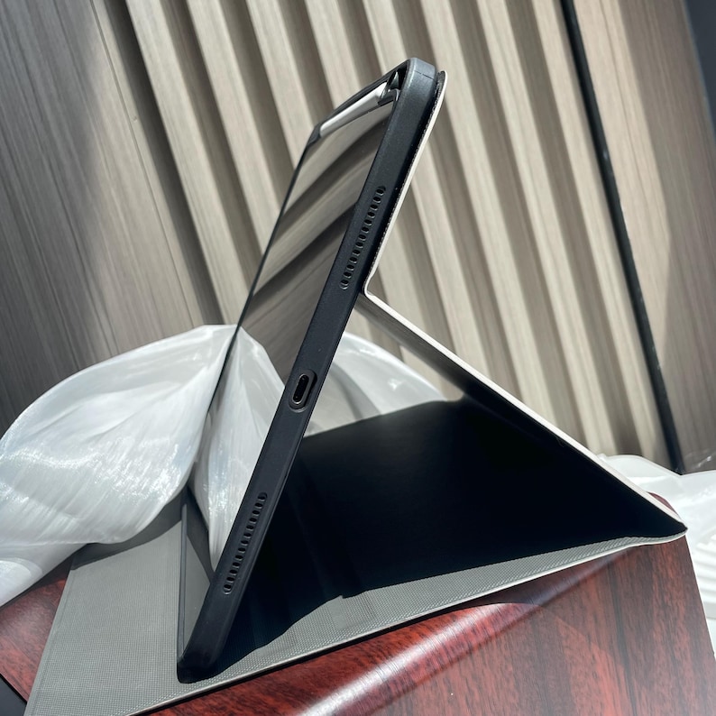 May include: A black iPad case with a built-in stand, shown in a folded position. The case is made of a durable material and has a sleek design.