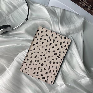 Puede incluir: Una funda para lector electrónico beige y negra con un diseño de manchas.