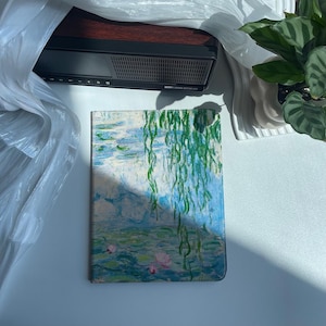 Puede incluir: Una cubierta de cuaderno con una pintura de nenúfares y sauces llorones en tonos azules, verdes y blancos.